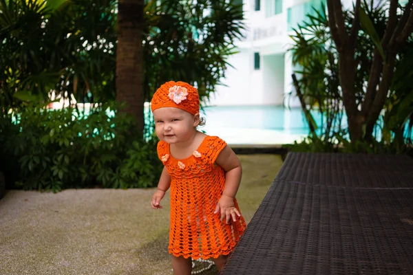 Uma menina em um vestido de malha laranja e chapéu é surpreendida, se alegra, grita, chora, levanta as mãos. conceito de moda infantil . — Fotografia de Stock