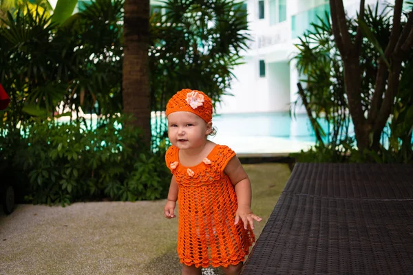 Uma menina em um vestido de malha laranja e chapéu é surpreendida, se alegra, grita, chora, levanta as mãos. conceito de moda infantil . — Fotografia de Stock