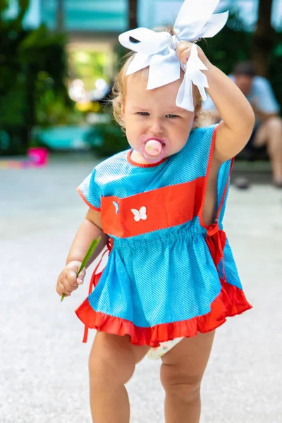 A girl in a blue dress with a white bow is surprised, rejoices, screams, cries, raises her hands. childrens fashion concept. — Stock Photo, Image