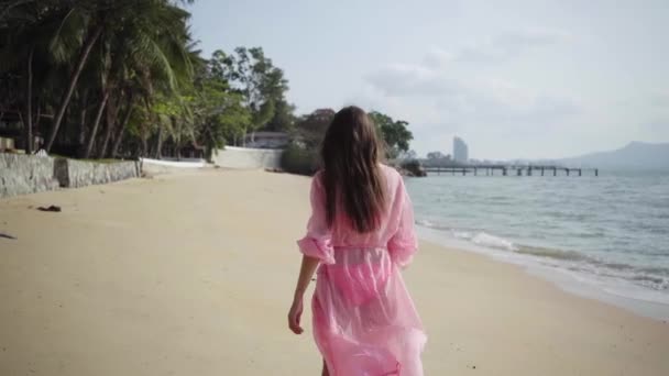 Bella femmina in un lungo vestito rosa in via di sviluppo cammina girando sulla spiaggia sulle rocce. primo piano. 4k . — Video Stock