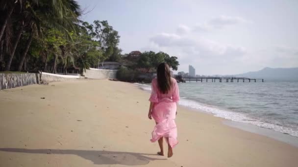 Mooie vrouw in een lange ontwikkeling van roze jurk wandelingen spinnen rondlopen op het strand op de rotsen. Close-up. 4k. — Stockvideo