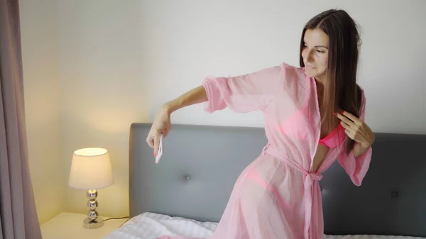 Menina em um roupão rosa transparente faz assaltos selfie na cama. 4k . — Fotografia de Stock