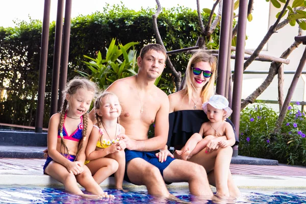 A large family sits by the pool in the villa. Mom, Dad and three daughters. The concept of a happy family, a large family.