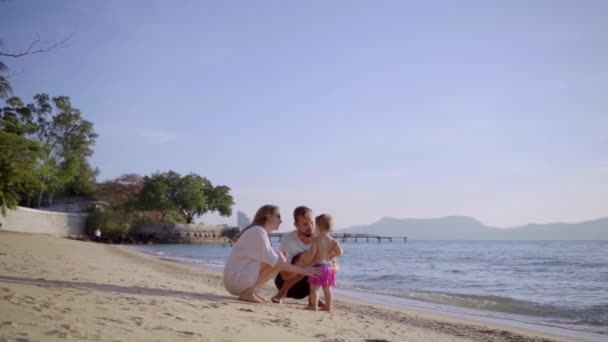 Una familia feliz en la playa, cogida de la mano, saludando a una niña. Mamá papá hija caminar en la playa. concepto de familia feliz. 4k — Vídeos de Stock