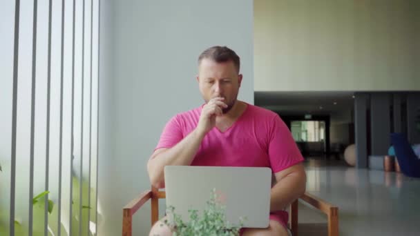 Slow motion shot of a man smoking an electronic cigarette, he works on a laptop. He looks at the screen of a laptop monitor and is engaged in vaping — Stock Video