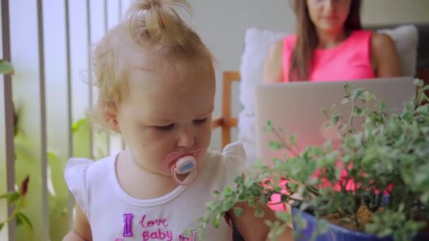 Mom フリーランサー作品コンピューターで Skype で話して、娘は退屈している鉢植えの植物、スローモーションを研究. — ストック動画