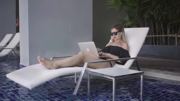 Freelancer kobieta siedzi na leżaku w pobliżu basenu i pracy na laptopie, zwolnionym tempie. — Wideo stockowe