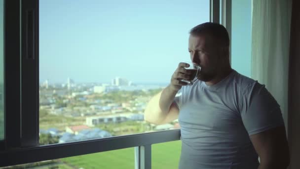 Férfi iszik kávét, és úgy néz ki, keresztül panoráma ablakkal mosolyog reggel, lassú mozgás — Stock videók