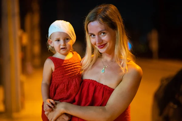 Madre tiene la figlia tra le braccia, la madre con la figlia è vestita con abiti rossi, il bambino con il basco bianco, di notte . — Foto Stock