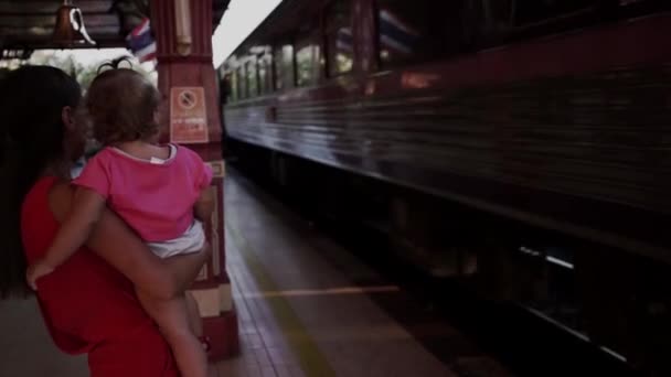 Moeder en kind staan op het station in Hua Hin, Thailand, en zwaaien naar de vertrek trein. Reizen met de trein met een kind. Slow Motion — Stockvideo