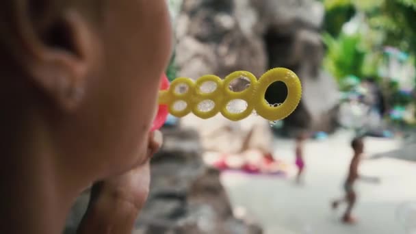 Vrouw blaast zeepbellen in de tuin, kinderen lopen in de achtergrond, slow-motion — Stockvideo