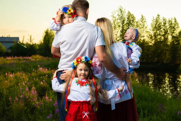 Large family in the ethnic Ukrainian costumes sit on the meadow, the concept of a large family. back view