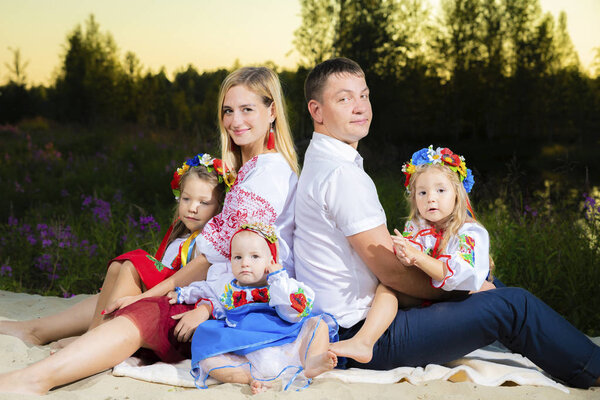 large family in ethnic Ukrainian costumes sit on the meadow, the concept of a large family.