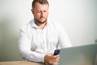 telefona işyerinde bilgisayarın yakınına bir masada oturan erkek Beyaz gömlekli görünüyor