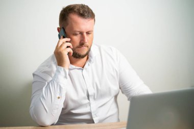 bilgisayarın yakınına bir masada oturan işyerinde telefonda konuşurken Beyaz gömlekli erkek