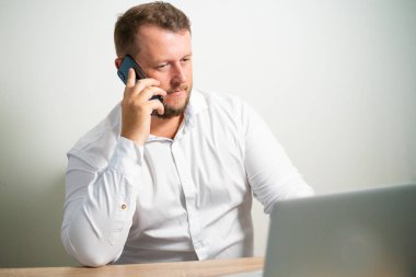 Beyaz gömlekli bilgisayarın yakınına bir masada oturan işyerinde telefonda konuşurken ciddi erkek