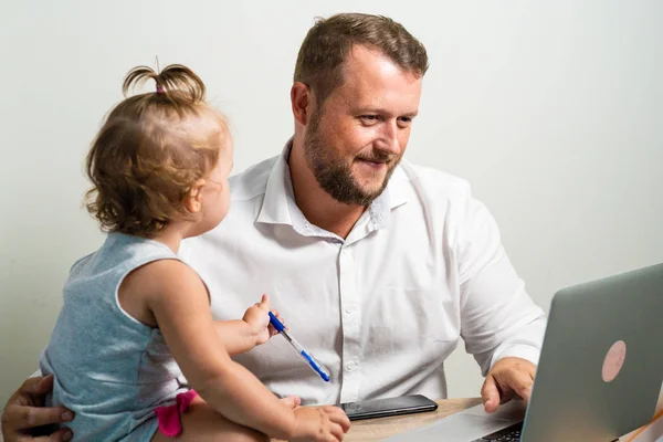 Freelancer work concept. Happy dad working at home with a laptop, holding the baby in his arms