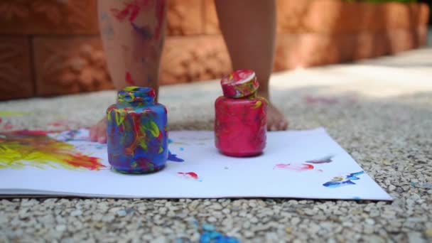 Pernas de criança desenha uma pintura de dedo - azul, vermelho e amarelo em uma folha branca. Desenvolvimento infantil criativo no jardim de infância ou tempo livre em casa. câmara lenta — Vídeo de Stock