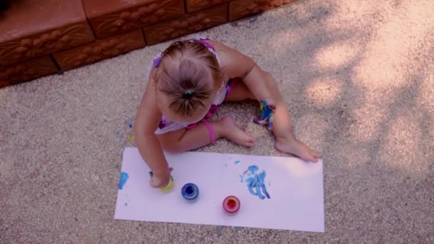 Όμορφο κοριτσάκι αντλεί με δακτυλομπογιές από ένα λευκό φύλλο χαρτί. Ανάπτυξη δημιουργικό παιδί στο νηπιαγωγείο ή ελεύθερο χρόνο στο σπίτι. αργή κίνηση. — Αρχείο Βίντεο