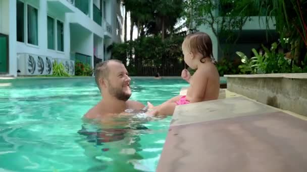 A cute little kid and his father having a swimming lesson in the pool. Father and daughter happily smiling and playing. Girl jumping to dad in her arms — Stock Video