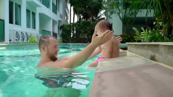 Egy aranyos kis gyerek és az apja, birtoklás egy medence lecke a medencében. Apa és lánya boldogan mosolyog és játszik. Lány apám karjaiban ugrás — Stock videók