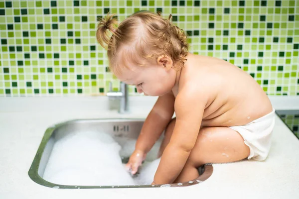 Baby im Waschbecken. Baby sitzt in der Spüle und berührt das Wasser aus dem Wasserhahn — Stockfoto