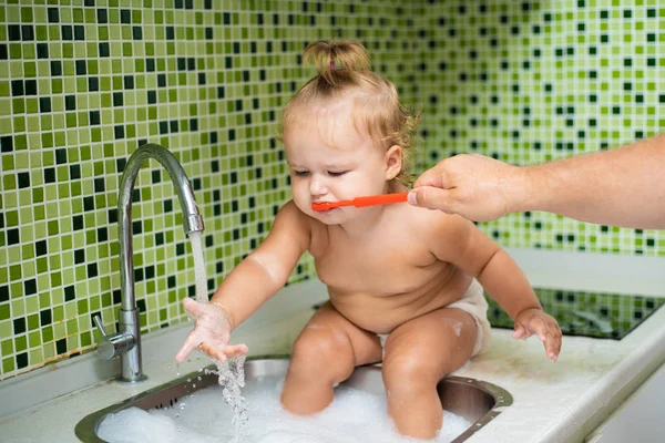 Söta barn girl borsta hennes tänder i badrummet. Söt baby sitter i diskhon. Pappa hjälper till att borsta barnets tänder — Stockfoto