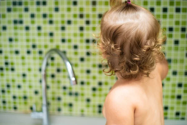 Baby im Waschbecken. Baby sitzt in der Spüle und berührt das Wasser aus dem Wasserhahn — Stockfoto