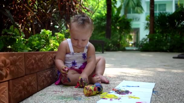 Όμορφο κοριτσάκι αντλεί με δακτυλομπογιές από ένα λευκό φύλλο χαρτί. Ανάπτυξη δημιουργικό παιδί στο νηπιαγωγείο ή ελεύθερο χρόνο στο σπίτι. αργή κίνηση. — Αρχείο Βίντεο