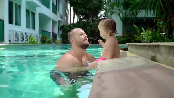 Un niño lindo y su padre teniendo una clase de natación en la piscina. Padre e hija felizmente sonriendo y jugando. Chica saltando a papá en sus brazos — Vídeos de Stock