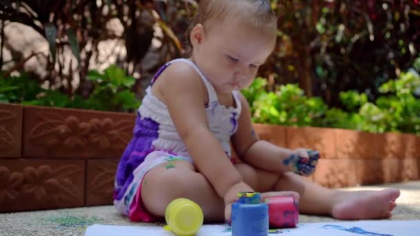 Красивая маленькая девочка рисует пальцами на белом листе бумаги. Творческое развитие ребенка в детском саду или свободное время дома. замедленное движение . — стоковое видео