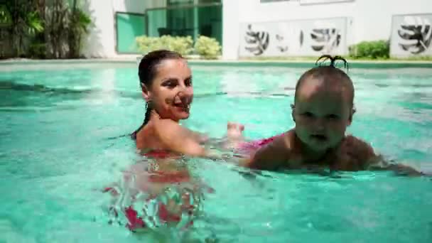 Sevimli küçük çocuk ve annesi havuzda yüzme dersi sahip. Anne arka plan ve tropikal palmiye ağaçlarının güneşli havalarda ellerinde tutar. — Stok video