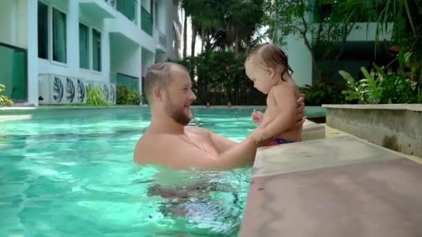 Un bambino carino e suo padre che fanno una lezione di nuoto in piscina. Padre e figlia sorridono e giocano felicemente. Ragazza che salta a papà tra le braccia — Video Stock