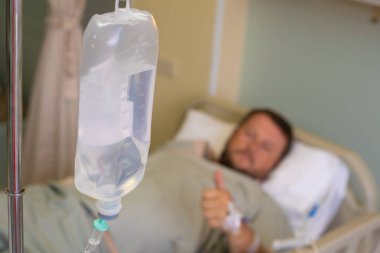 Close. Hastanede kemoterapi sırasında damlalıklı erkek eli. Adam hastane odasında, odaklanmadan. Sağlık sağlık ve şifa bir konudur.