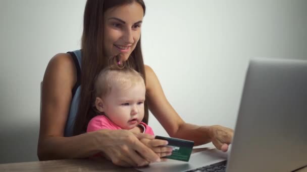 Compras concepto en línea. Mujer e hija sosteniendo una tarjeta de crédito y utilizando un ordenador portátil. mujer y niño pagan compras en línea — Vídeos de Stock