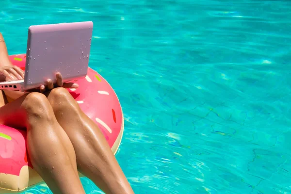 Повітряний вид на молоду брюнетку, що плаває на надувному великому пончику з ноутбуком у прозорому бірюзовому басейні, крупним планом — стокове фото