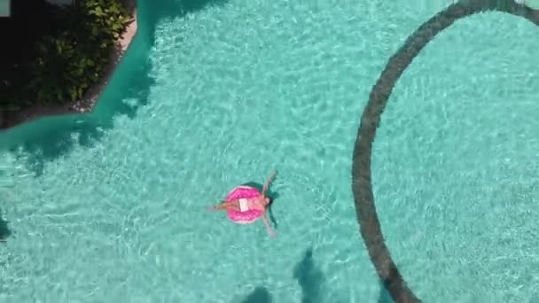 Молодая женщина плавает в море в круге плавания. Девушка отдыхает в бассейне на надувном круге с компьютером, вид сверху — стоковое видео