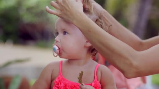 Женщина делает прическу для своей маленькой дочери, завязывая ей волосы. Концепция моды, материнства, красоты — стоковое видео