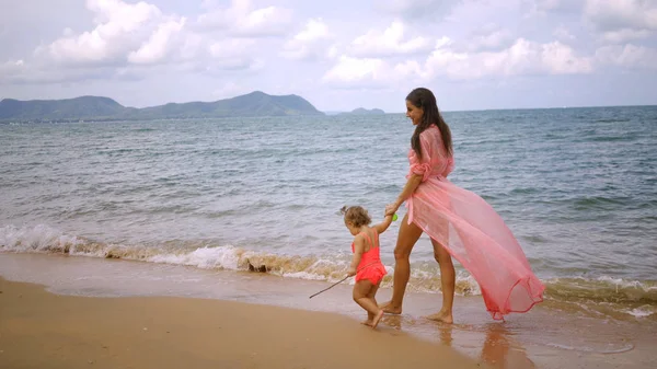 Мать и дочь в розовых платьях прогуливаются вдоль красивого побережья. концепция материнства, счастливое детство, мода, праздники — стоковое фото
