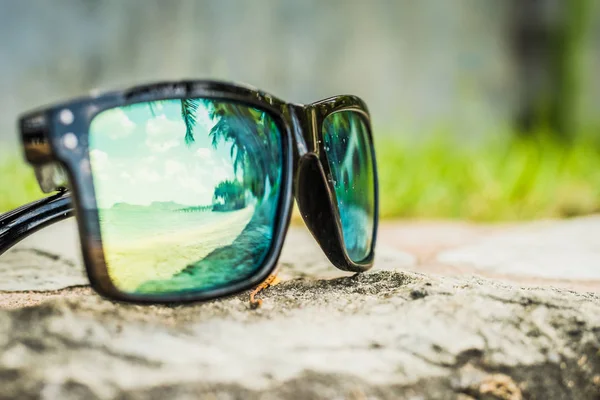 Fashionable sunglasses. Sunglasses with mirrored lenses. Reflection of the beach and tropical palm trees in sunglasses