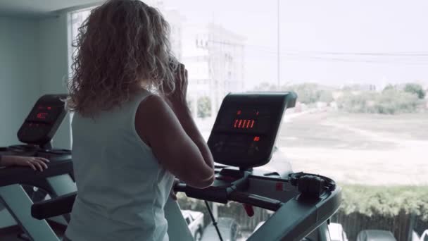 Senior kvinna är engagerad på ett löp band i gymmet. kvinnliga pratar i telefon gör löp bandet — Stockvideo