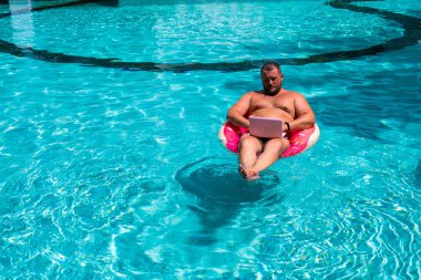 Havuzda suda şişme halkası olan erkek bir işadamı. Pembe Laptop ile Yüzme Daire Komik Fat Man. serbest kavram.