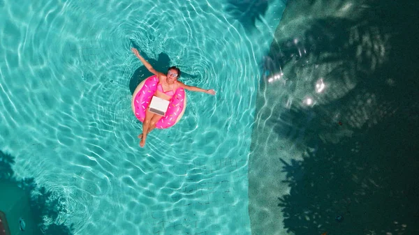 Gyönyörű fiatal nő egy rózsaszín laptop egy felfújható gyűrűt a vízben a medencében. a freelancing, az üzleti és az utazási koncepció. Légifelvétel — Stock Fotó
