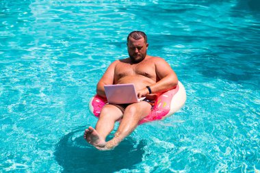 havuzda suda şişme halka ile erkek bilgisayarda çalışır. Pembe laptop ile yüzme daire komik şişman adam. serbest kavramı
