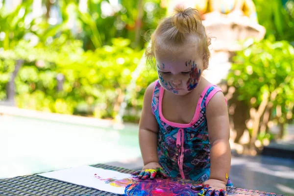 Pequena menina tintas com pinturas de dedo perto da piscina . — Fotografia de Stock