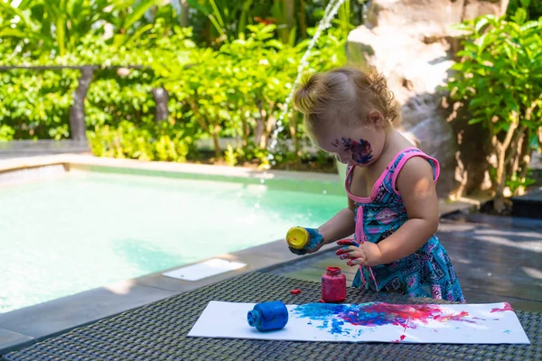 Pequena menina tintas com pinturas de dedo perto da piscina . — Fotografia de Stock