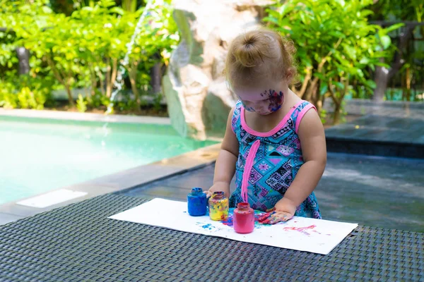 Pequena menina tintas com pinturas de dedo perto da piscina . — Fotografia de Stock