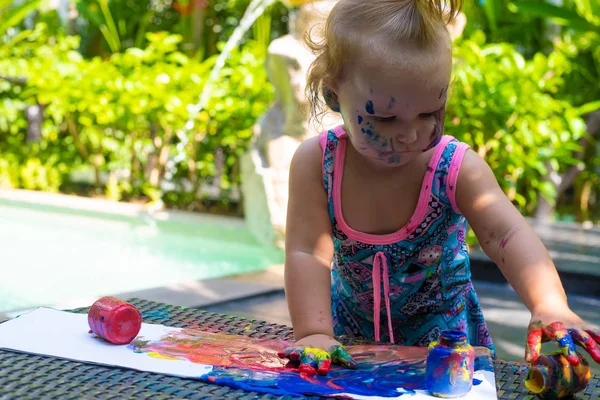 Pequena menina tintas com pinturas de dedo perto da piscina . — Fotografia de Stock