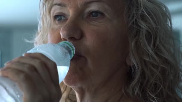 Femme âgée boit de l'eau potable dans la salle de gym, gros plan — Video