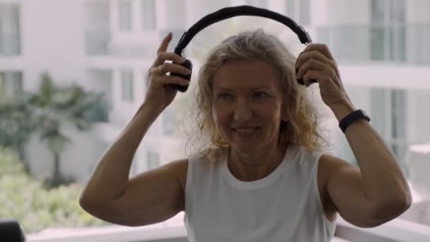 Senior kvinna är engagerad i gymmet. blond kvinna lyssnar på musik på hörlurar i gymmet — Stockvideo